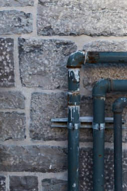 Çekiçle yontulmuş granit duvar ve yeşil metal borularla harç.