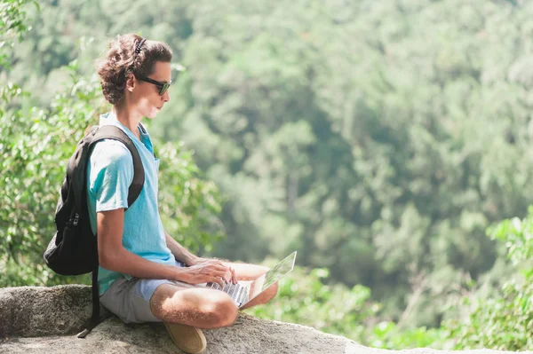 Homem freelancer está sentado no topo da montanha e trabalhando em laptop — Fotografia de Stock