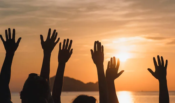 Many hands raised against sunset sky