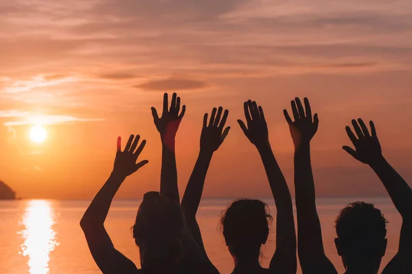 Many hands raised against sunset sky