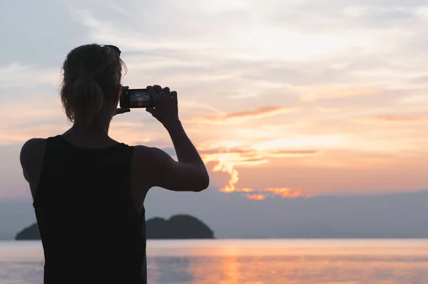 Man taking photo in picturesque sea scenery at sunset