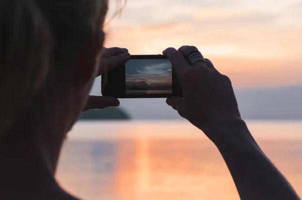 Man taking photo in picturesque sea scenery at sunset