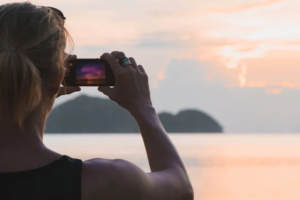 Man taking photo in picturesque sea scenery at sunset