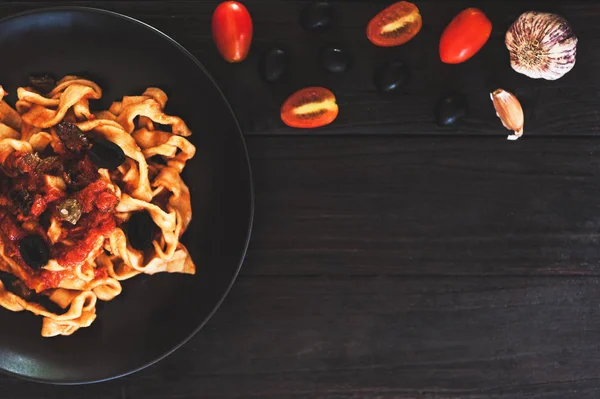 Italienische Küche. Nudeln mit Olivenöl, Knoblauch, Basilikum und Tomaten. Spaghetti mit Tomaten auf schwarzem Holz Hintergrund — Stockfoto