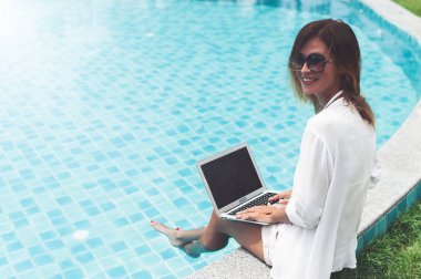 Dizüstü bilgisayarında çalışan bir kadın havuz kenarında oturuyor.