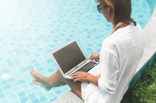 Жінка працює на своєму ноутбуці, сидячи біля басейну — стокове фото