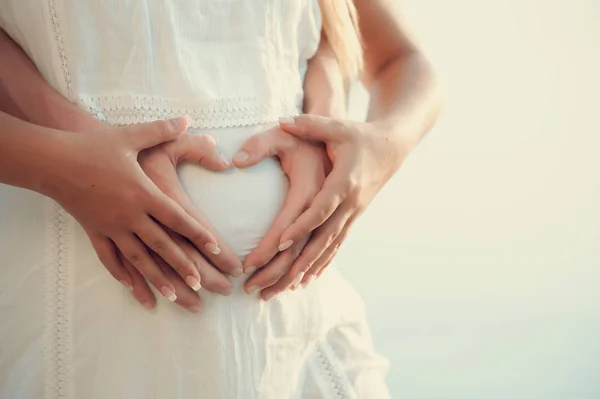 Mãos dos pais fazendo uma forma do coração na barriga da mãe grávida — Fotografia de Stock