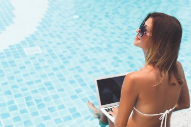 Dizüstü bilgisayarında çalışan bir kadın havuz kenarında oturuyor.