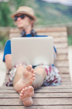 Laptop ve kulaklık ile plajda çalışan yakışıklı sarışın adam