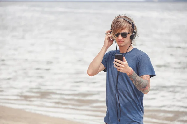 Retrato de jovem em fones de ouvido e óculos de sol na praia — Fotografia de Stock