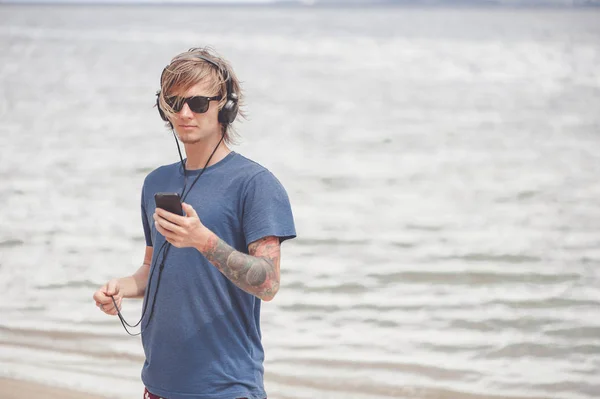 Retrato de jovem em fones de ouvido e óculos de sol na praia — Fotografia de Stock