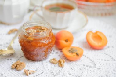 Bir cam kasede beyaz zemin üzerinde bir sepet içinde taze kayısı kayısı reçeli