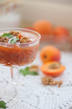 Bir cam kasede beyaz zemin üzerinde bir sepet içinde taze kayısı kayısı reçeli