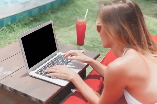Молода фрілансерка лежить біля басейну і працює над своїм ноутбуком . — стокове фото