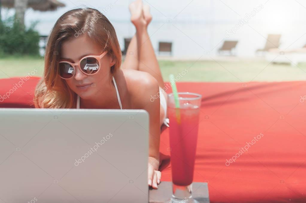 Young female freelancer laying near the pool and working on her laptop.
