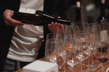Erkek şarap garsonu kırmızı şarabı uzun saplı şarap bardaklarına dolduruyor..