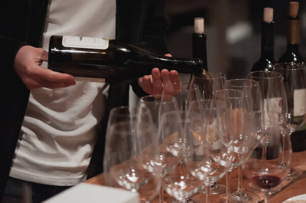 Male sommelier pouring red wine into long-stemmed wineglasses.