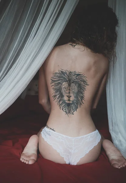 Γυμνή πλάτη με το τατουάζ λιοντάρι του μια νεαρή γυναίκα που κάθεται σε ένα κρεβάτι — Φωτογραφία Αρχείου