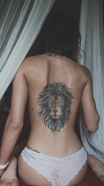 Espalda desnuda con el tatuaje de un león de una joven sentada en una cama — Foto de Stock