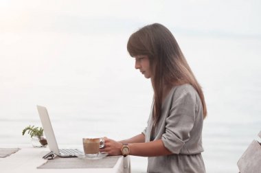 Genç ve güzel bir kız bir kafede oturuyor ve bilgisayarla çalışıyor.