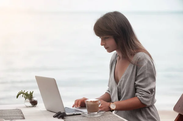 Junges schönes Mädchen sitzt in einem Café und arbeitet am Computer — Stockfoto