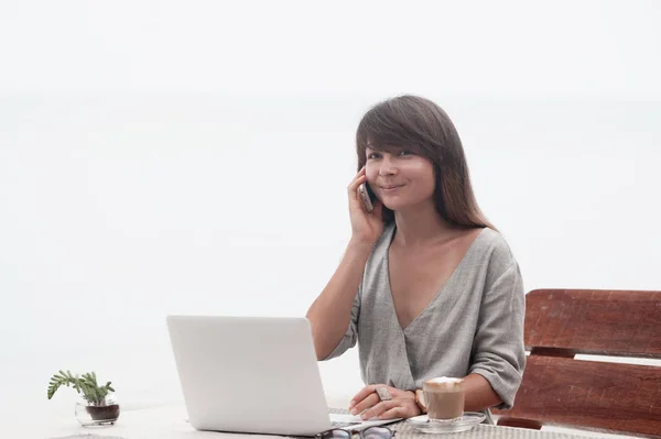 Junges schönes Mädchen sitzt in einem Café mit einem Laptop und spricht auf der Pnone — Stockfoto