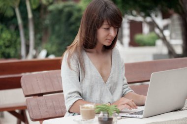 Açık havada bir kafede oturan ve bilgisayarda çalışan genç güzel kız