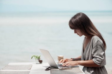 Genç ve güzel bir kız bir kafede oturuyor ve bilgisayarla çalışıyor.