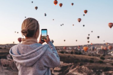 Kapadokya 'da gün doğumunda fotoğraf çeken güzel manzara ve balonlar çeken bir kadın..