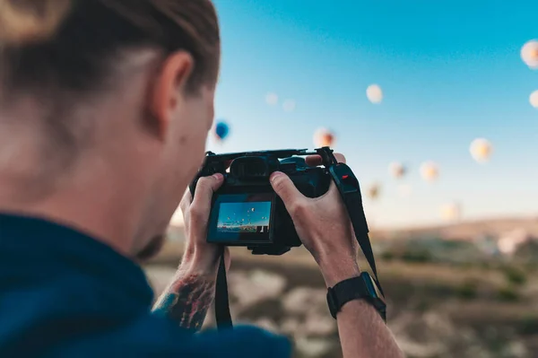 Fiatal férfi fotós képeket készít léggömbökről napkeltekor Cappadociában — Stock Fotó