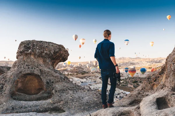 Jovem fotógrafo em férias na Turquia Capadócia olhando para os balões de ar durante o nascer do sol em Kapadokya — Fotografia de Stock