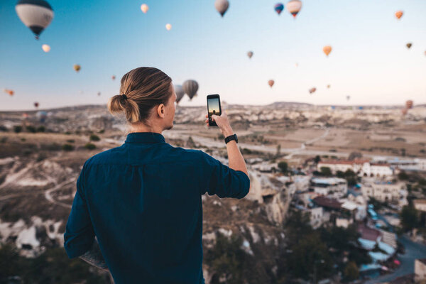 Man taking photo of beautiful landscape and balloons in Cappadocia with mobile camera, sunrise time.