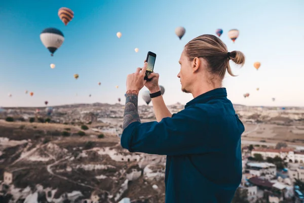 Mężczyzna robi zdjęcie pięknego krajobrazu i balonów w Kapadocji z aparatem mobilnym, czas wschodu słońca. — Zdjęcie stockowe