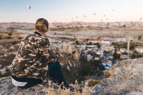 Young man sitting on a high and looking at the air balloons in Cappadocia