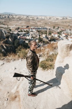 Kamuflaj elbiseli erkek avcı av tüfeğiyle avlanmaya hazır.