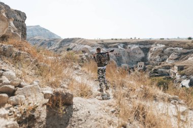 Kamuflaj elbiseli erkek avcı av tüfeğiyle avlanmaya hazır.