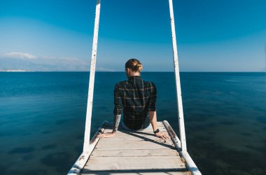 Rıhtımda oturan adam göle bakıyor.