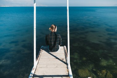 Rıhtımda oturan adam göle bakıyor.