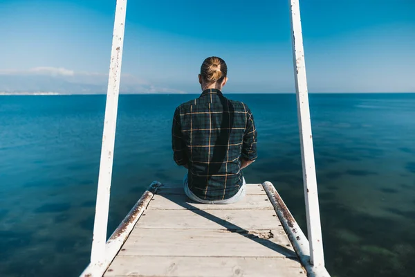 O homem está sentado no cais a olhar para o lago. — Fotografia de Stock