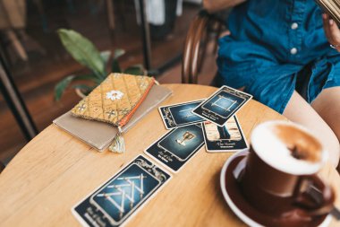 Kadın kafede masada Tarot kartları okuyor.