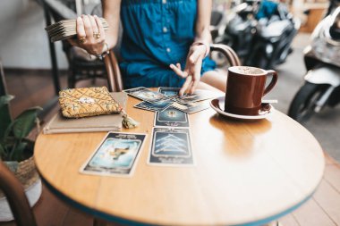 Kadın kafede masada Tarot kartları okuyor.