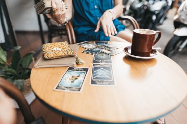 Kadın kafede masada Tarot kartları okuyor.