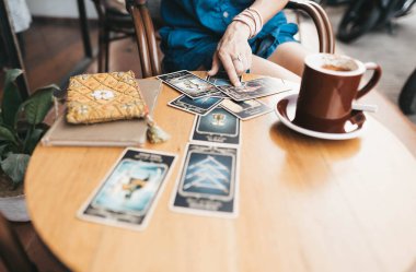 Kadın kafede masada Tarot kartları okuyor.