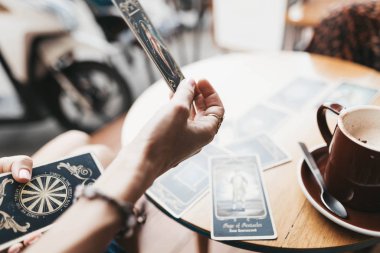 Kadın kafede masada Tarot kartları okuyor.