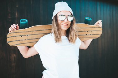 Güneş gözlüklü ve şapkalı çekici bir kadın duvarda duruyor.