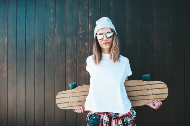 Güneş gözlüklü ve şapkalı çekici bir kadın duvarda duruyor.