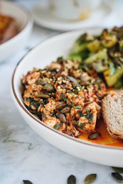 Kabak çekirdekli soya peyniri, salatalıklı avokado salatası ve mermer arka planda çavdar ekmeği ile servis edilen bazilika.