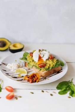 Ezilmiş avokadoyla sandviç ve beyaz arka planda domatesli haşlanmış yumurta.
