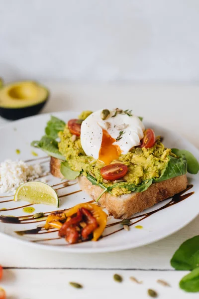 Ezilmiş avokadoyla sandviç ve beyaz arka planda domatesli haşlanmış yumurta.