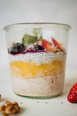 Sağlıklı diyet kahvaltı. Chia tohumlu yulaf ezmesi, beyaz arka planda cam bir kavanozda meyve ve fındık. Yan görünüm